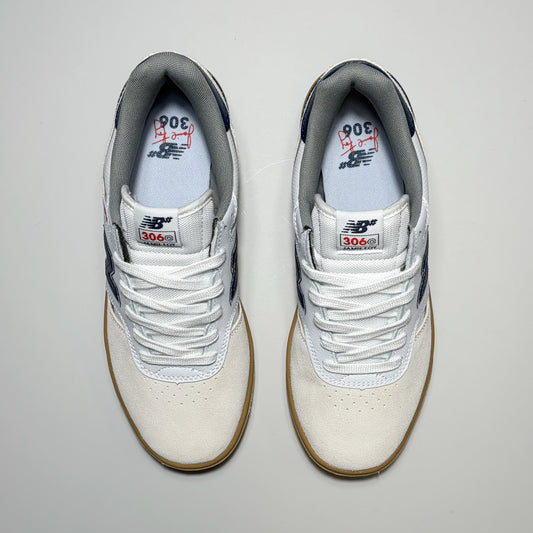 A pair of New Balance Numeric NM306C sneakers shown from a top-down view on a light gray background. The shoes feature an off-white suede and mesh upper, white laces, navy blue accents on the heel and tongue, and a brown gum sole.