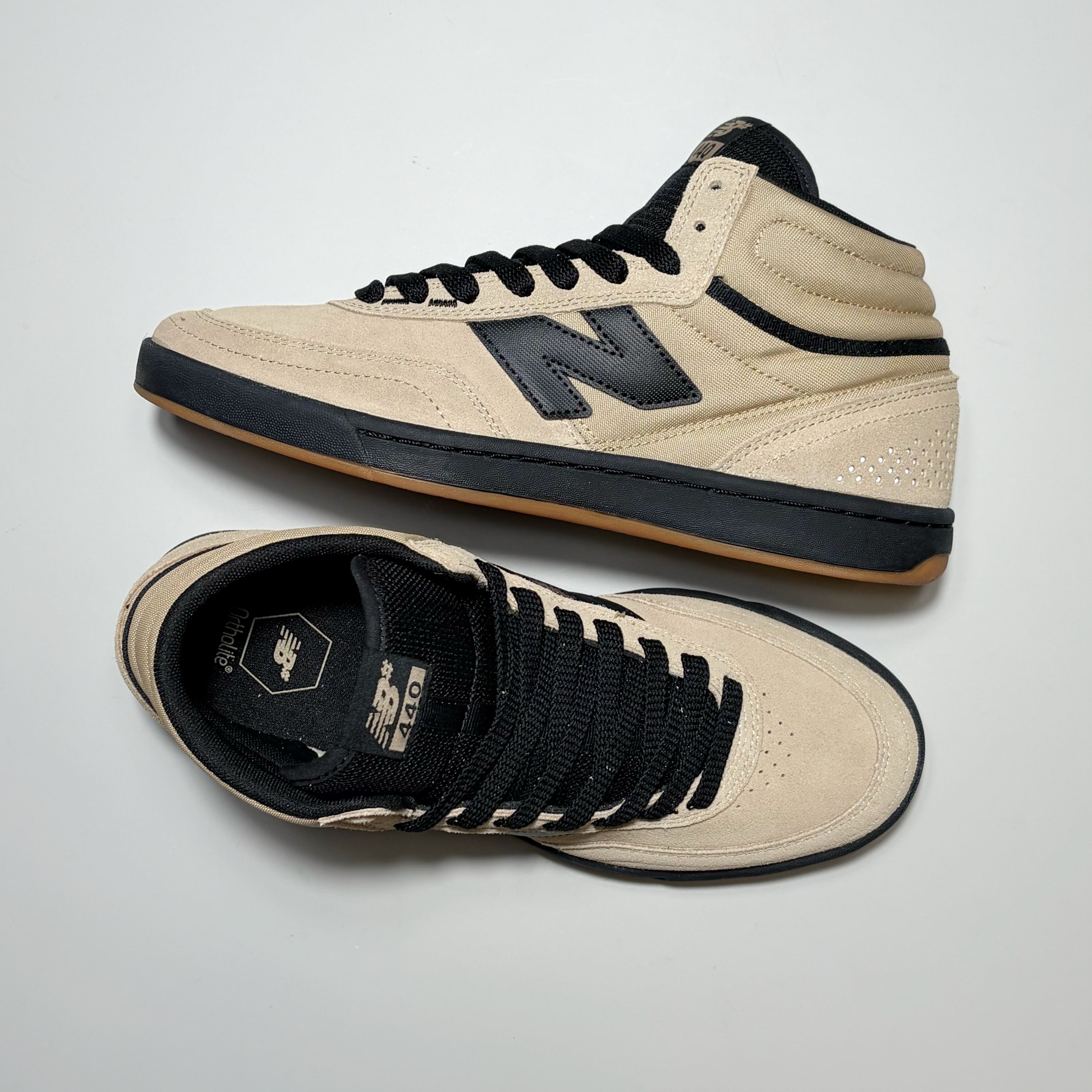 A pair of New Balance Numeric NM440 high-top skate shoes in beige and black, displayed on a light gray background. One shoe is shown from the side profile, highlighting the beige suede upper, black laces, and black 'N' logo, while the other is shown from the top-down view displaying the beige suede toe box, black collar, and black laces.