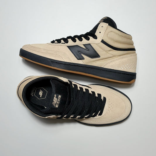 A pair of New Balance Numeric NM440 high-top skate shoes in beige and black, displayed on a light gray background. One shoe is shown from the side profile, highlighting the beige suede upper, black laces, and black 'N' logo, while the other is shown from the top-down view displaying the beige suede toe box, black collar, and black laces.