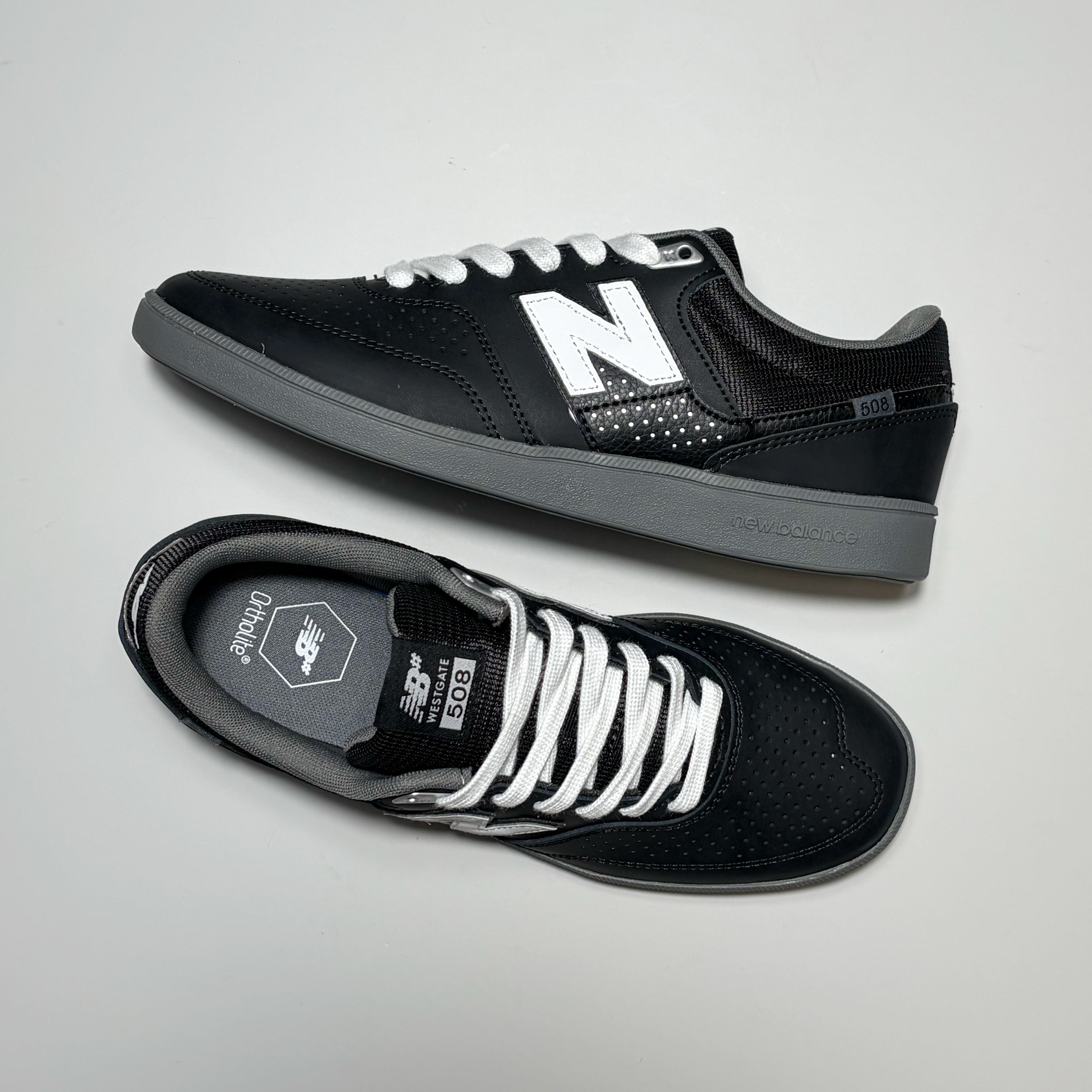 A pair of New Balance 508 sneakers, one on its side the other toe down view with white laces on grey background.