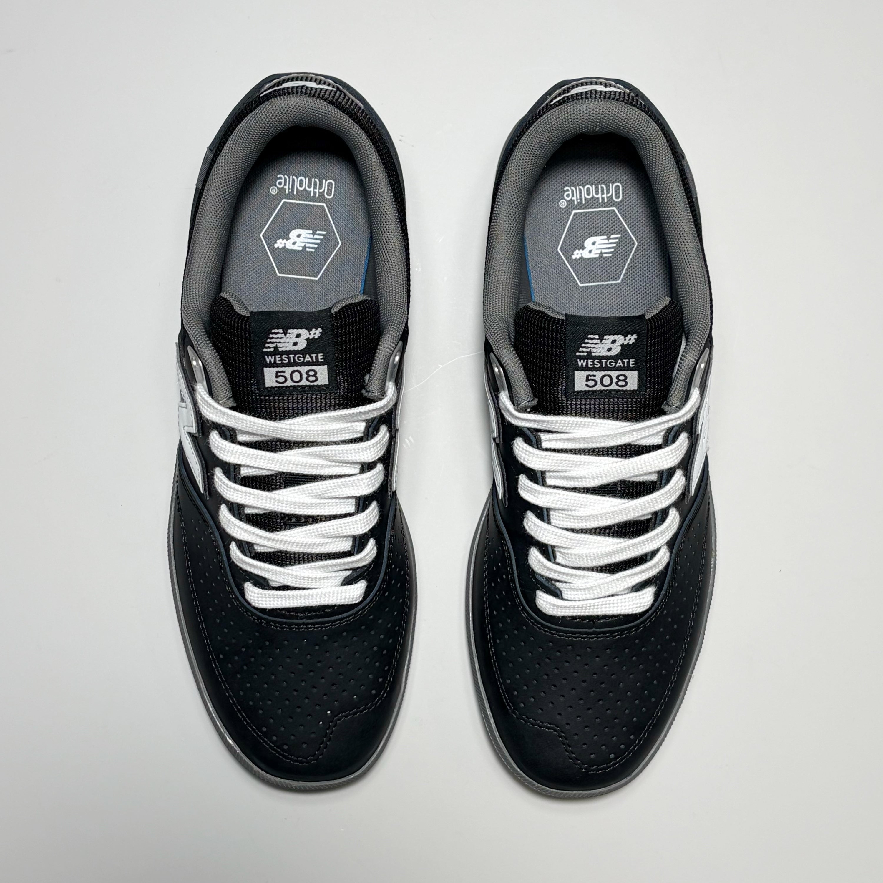 A pair of New Balance 508 Westgate signature sneakers shown from a top-down view. The shoes are primarily black with white laces, white side stripes, and a gray interior lining.