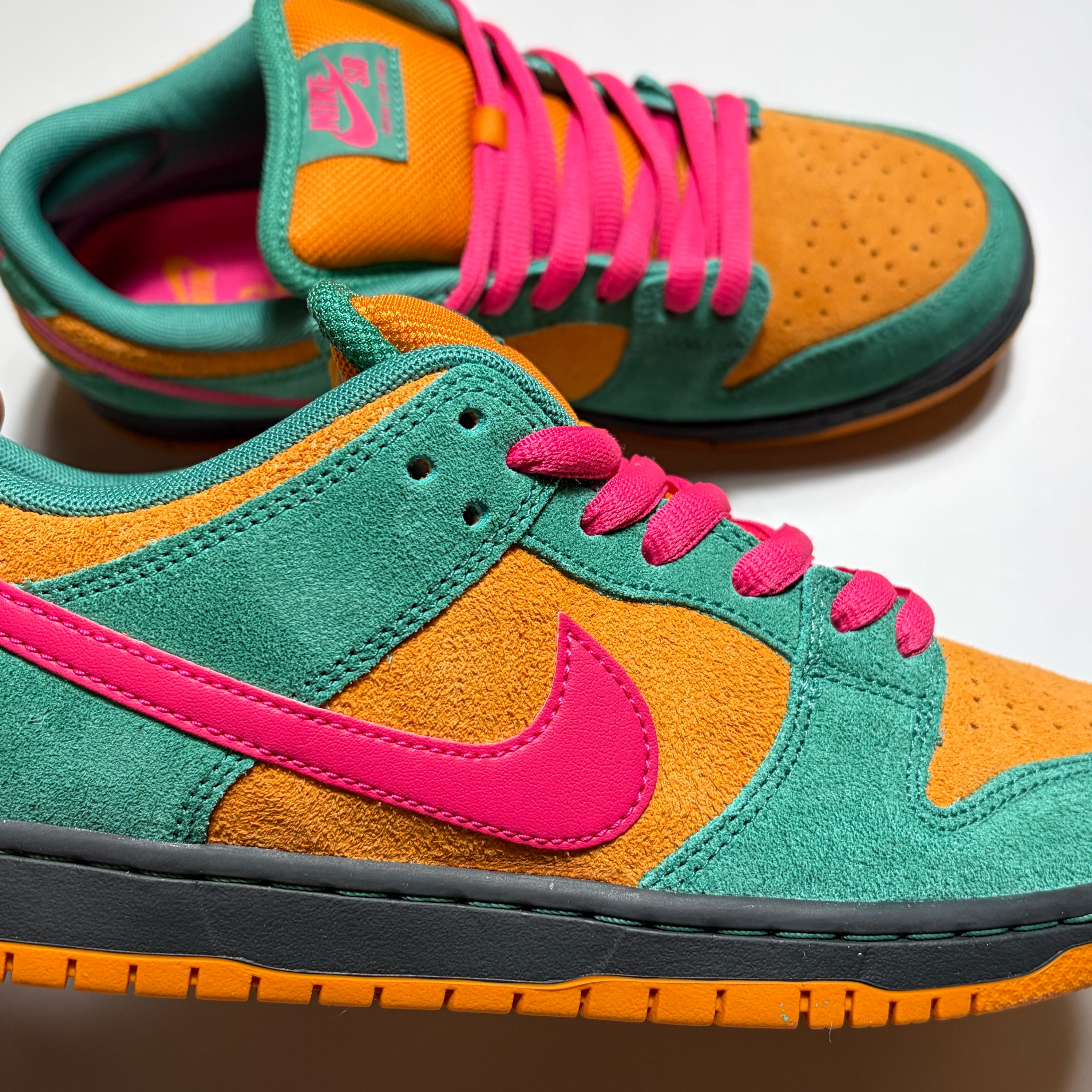 A pair of Nike SB Dunk Low sneakers in a vibrant green, orange, and hot pink colorway, featuring suede and mesh panels with matching colored laces and a black midsole.