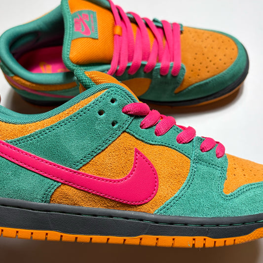 A pair of Nike SB Dunk Low sneakers in a vibrant green, orange, and hot pink colorway, featuring suede and mesh panels with matching colored laces and a black midsole.