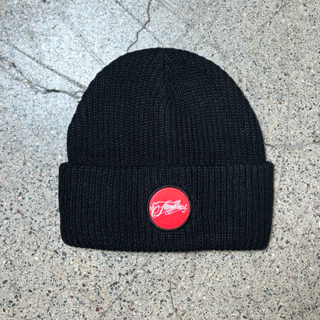 Full image of black beanie with folded  cuff. Red woven familia patch centered.