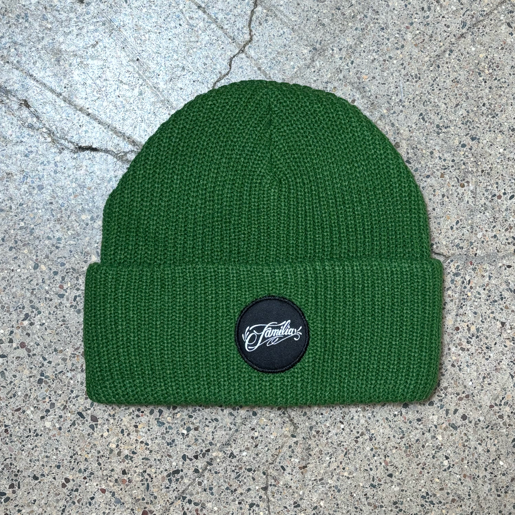 Full image of green beanie with folded  cuff. Black woven familia patch centered.