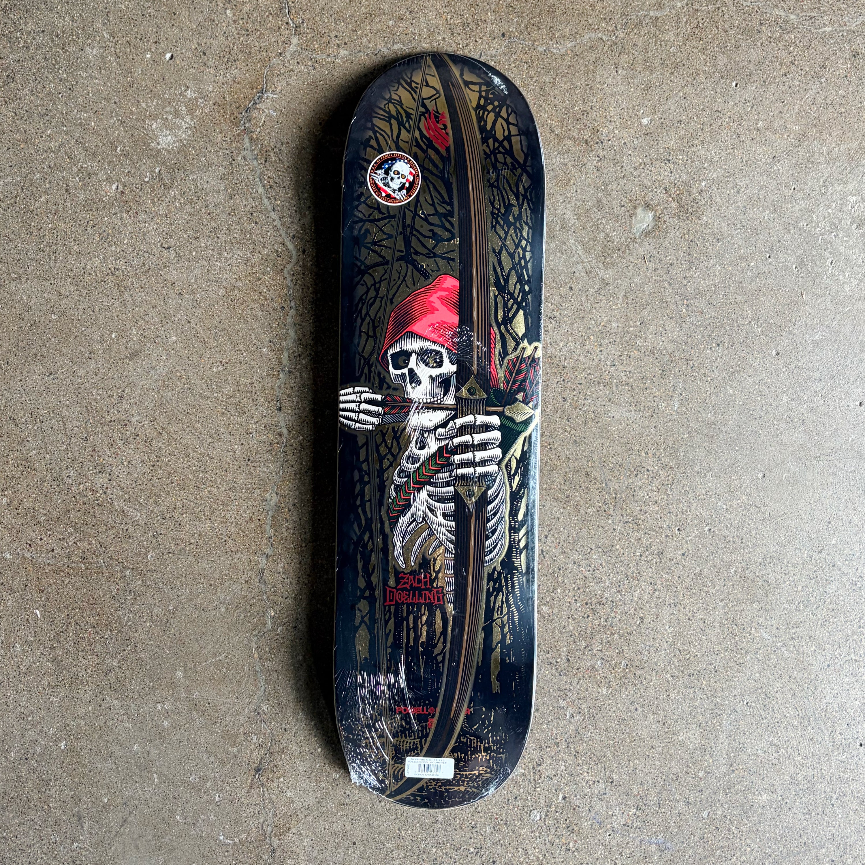 A Powell Flight Zach Doelling deck featuring a detailed graphic of a skeleton wearing a red hat, holding a bow and arrow, set against a dark forest background. The deck is photographed flat on a textured concrete floor