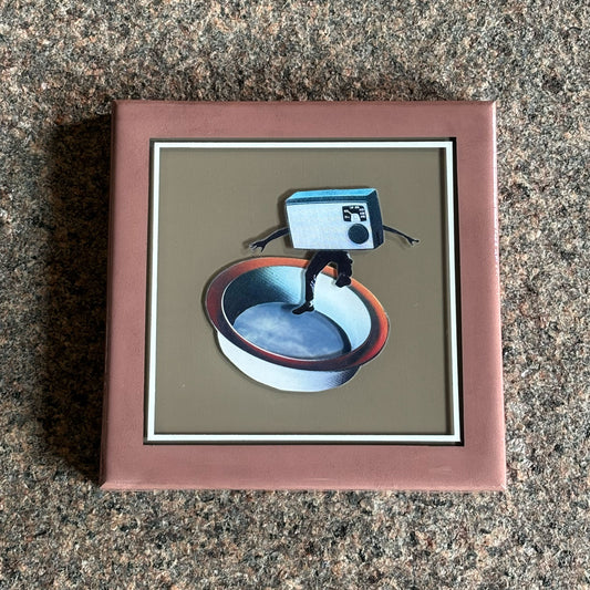 Framed artwork of a camera and bowl on a textured surface