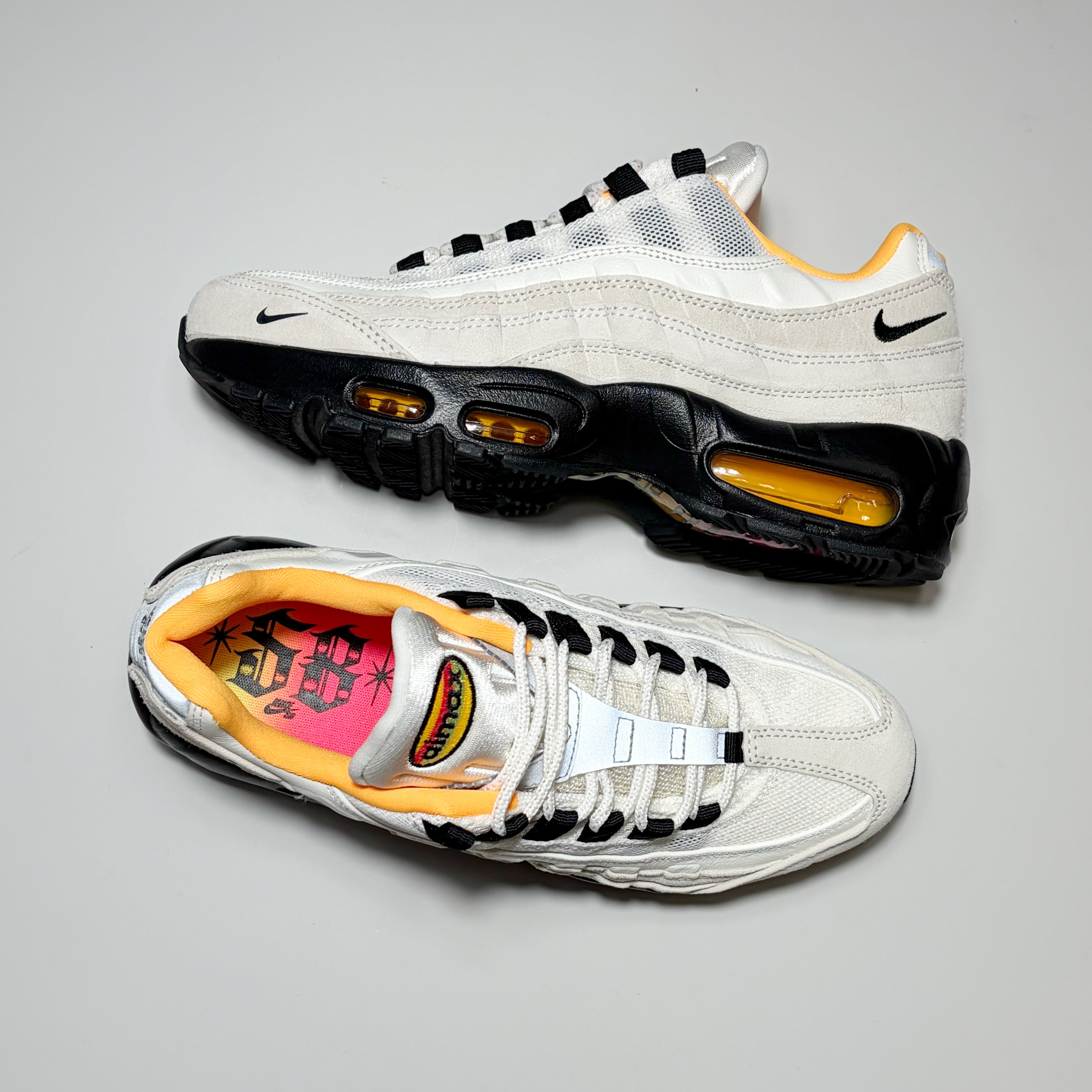 A pair of Nike Air Max 95 sneakers in white, black, and yellow, displayed from both the top and side profiles on a neutral gray background.