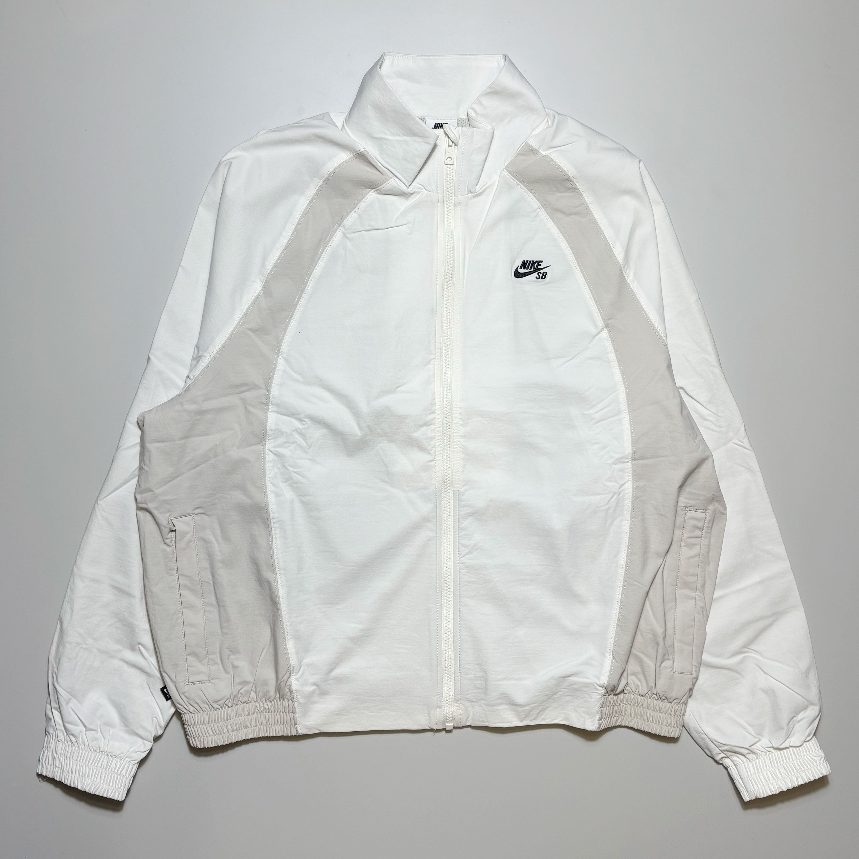 Front image of white/bone color blocked track jacket with full zip and nike sb logo embroidered on chest