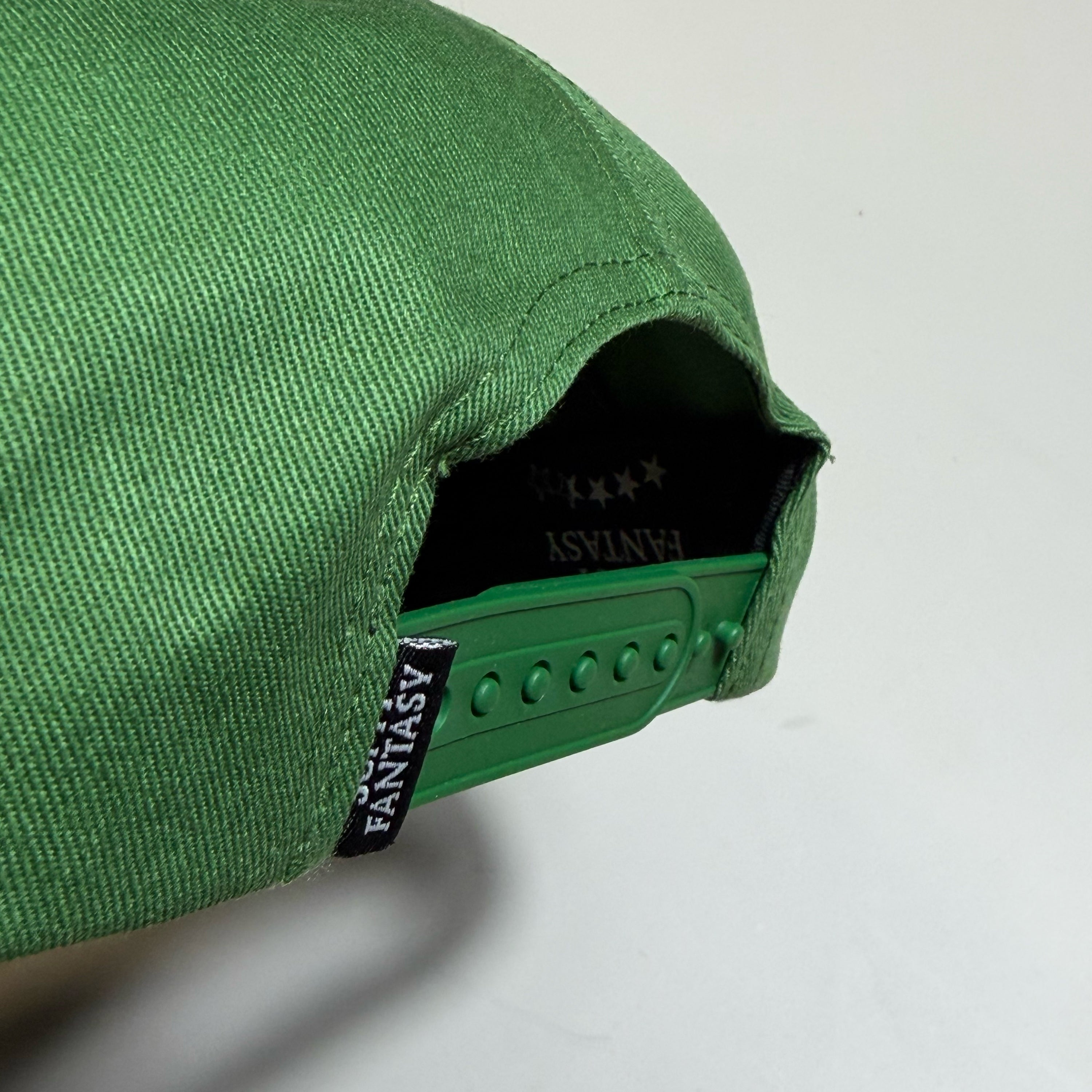 Close-up of a green baseball cap showing the fabric texture, the green adjustable strap, and the black interior lining with white FANTASY branding.