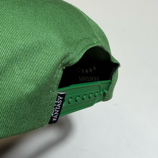 Close-up of a green baseball cap showing the fabric texture, the green adjustable strap, and the black interior lining with white FANTASY branding.