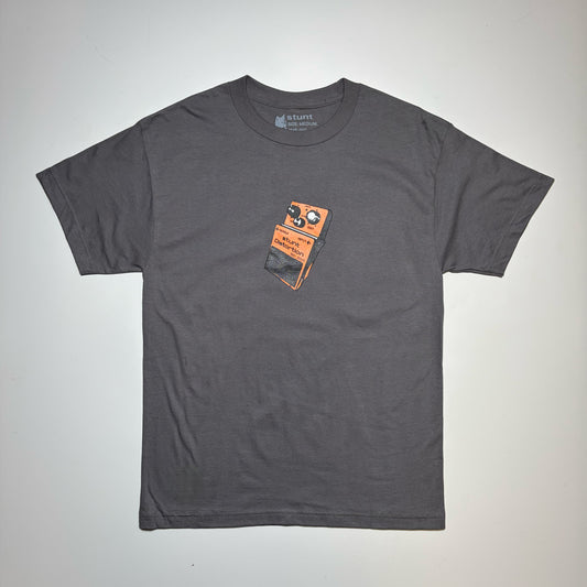 A dark gray crewneck t-shirt featuring a graphic print of an orange and black guitar effects pedal on the center chest, laid flat against a light gray background.