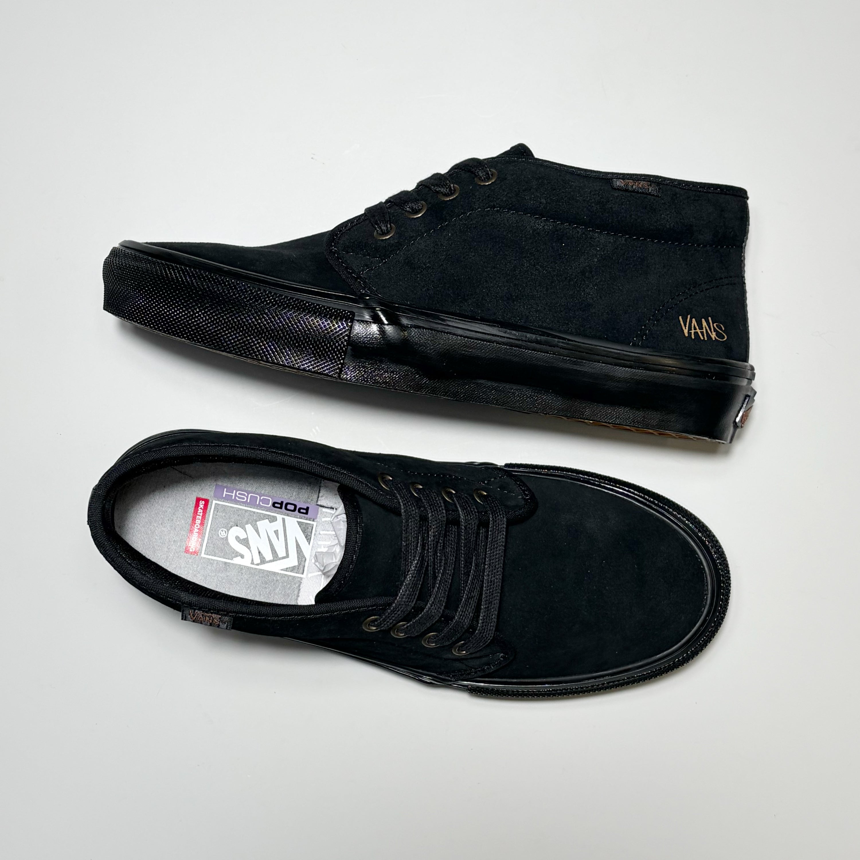A pair of black Vans Skate Chukka suede low-top sneakers, one shown from the side profile and the other from the top-down view, on a light gray background. Part of the Atiba Jefferson collection.
