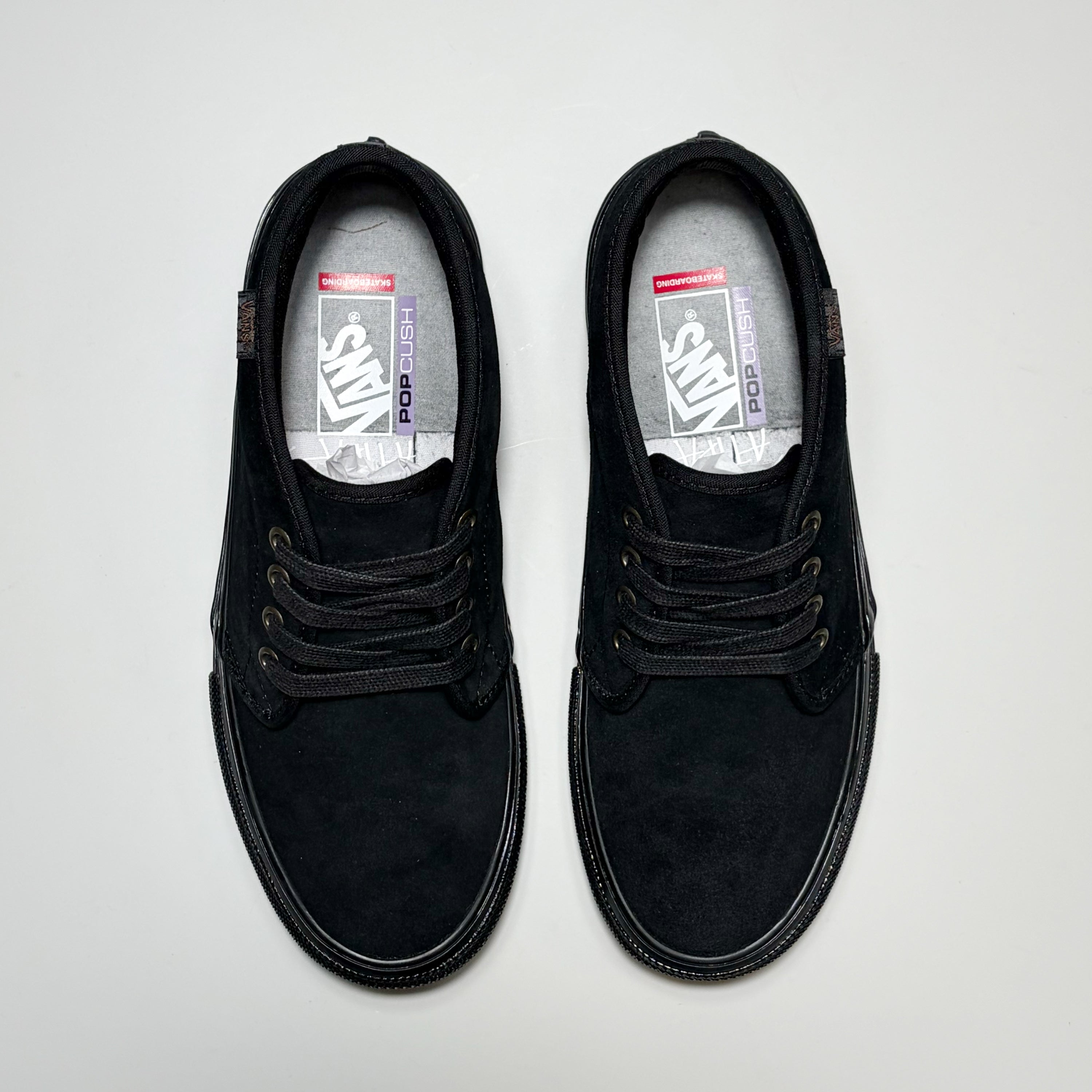 A pair of black Vans Skate Chukka low-top lace-up shoes shown from a top-down view on a light gray background. The shoes feature a suede-like finish, black laces, and a visible Vans logo on the insoles. Atiba Jefferson Collection 