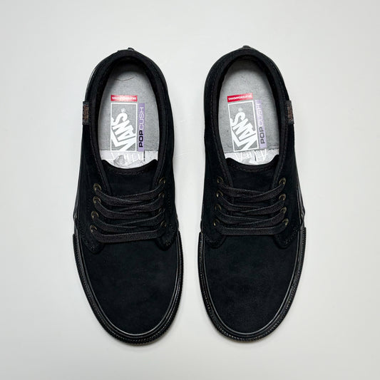 A pair of black Vans Skate Chukka low-top lace-up shoes shown from a top-down view on a light gray background. The shoes feature a suede-like finish, black laces, and a visible Vans logo on the insoles. Atiba Jefferson Collection 