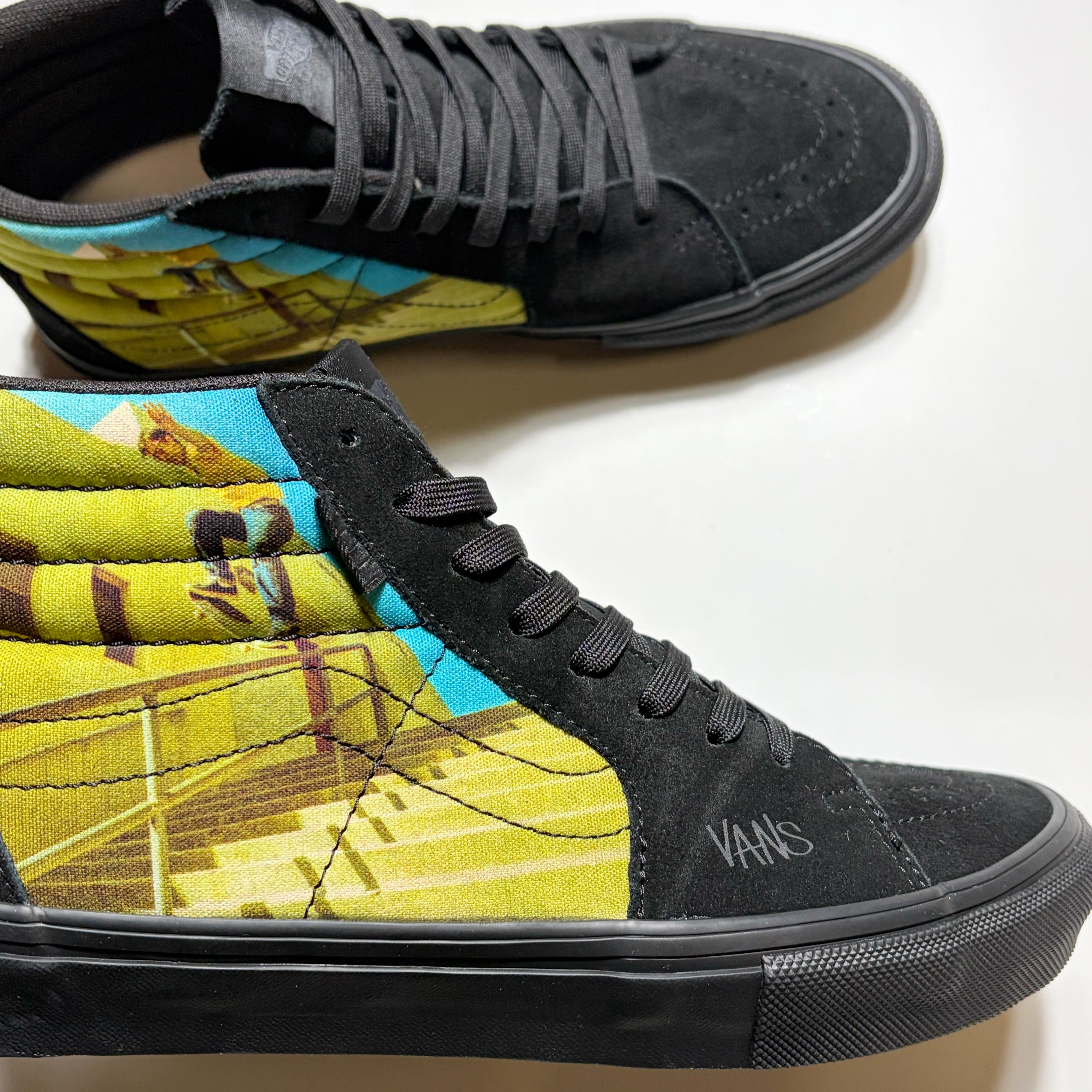 A pair of black high-top Vans sneakers with a colorful graphic print on the side panels, featuring a skateboarder Geoff Rowley on a staircase. Part of the Atiba Jefferson Collection.