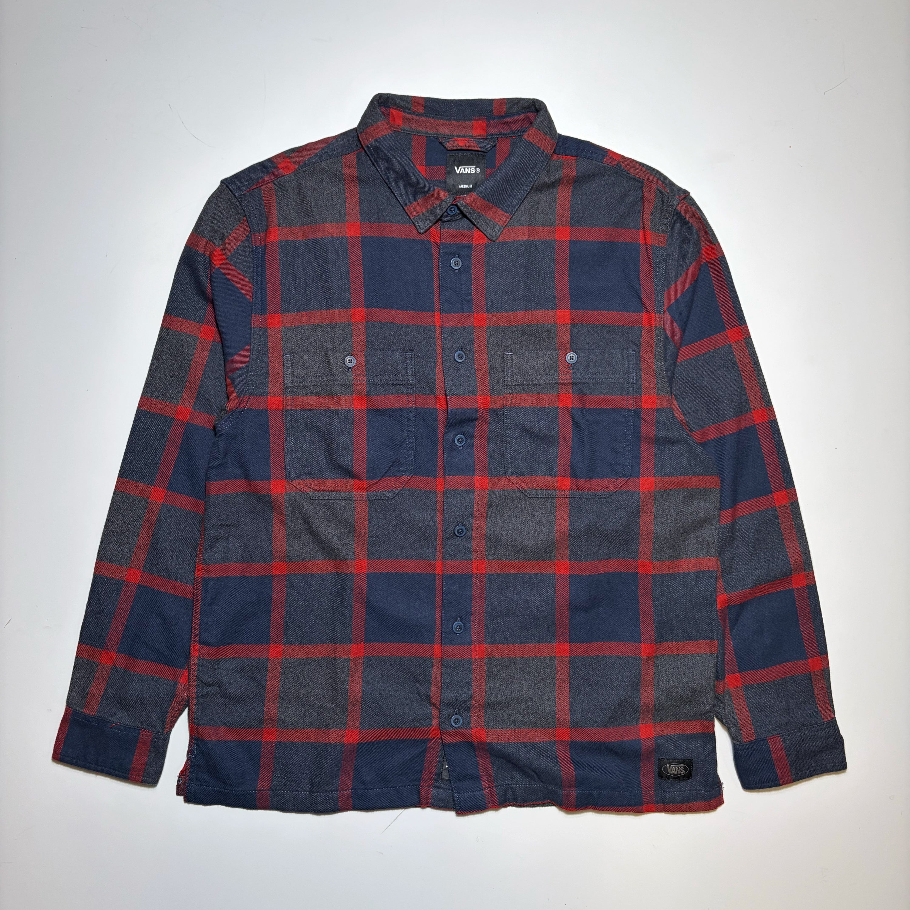 A vintage Vans button-down flannel shirt with a red and navy blue plaid pattern, laid flat against a light gray background.