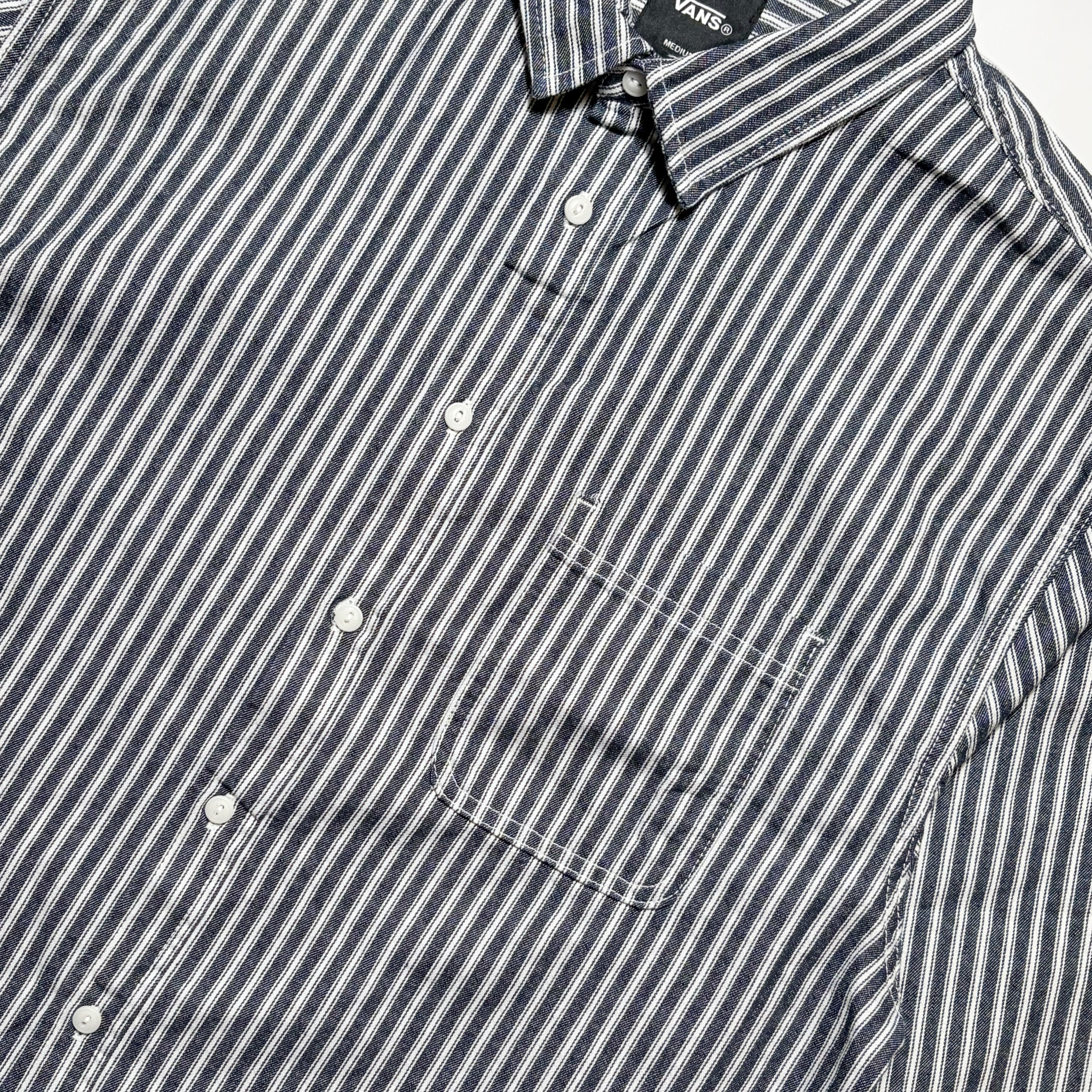 Close-up of a Vans button-down shirt with navy and white vertical stripes, featuring a chest pocket and white buttons.