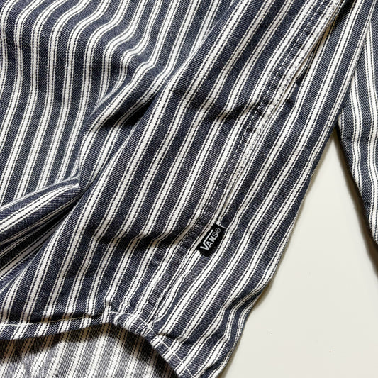 Close-up of a striped garment, likely a shirt or jacket sleeve, featuring vertical navy, white, and gray stripes with a small black Vans logo tag.