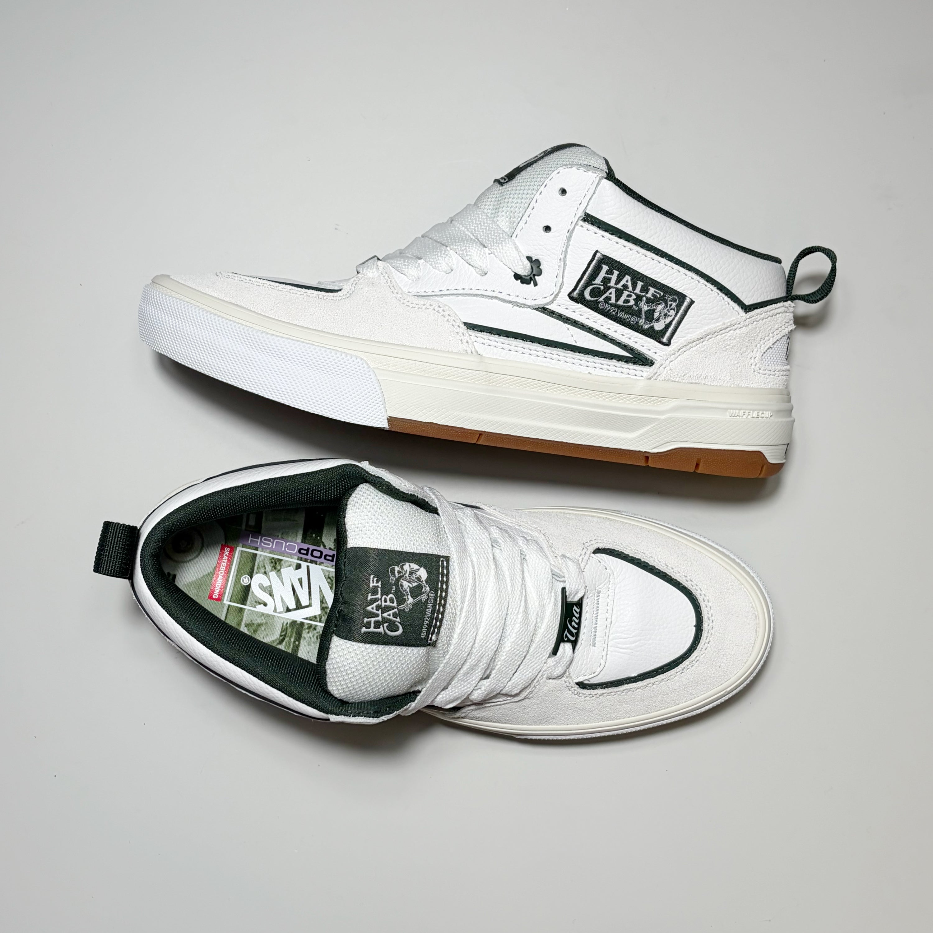 A pair of white Vans Skate Half Cab Wafflecup Una Farrar sneakers shown from different angles on a light gray background. One shoe is positioned upright, showing the side profile with its signature black stripe and Cactus patch, while the other is laid flat, showing the top view with white laces and a black tongue label.