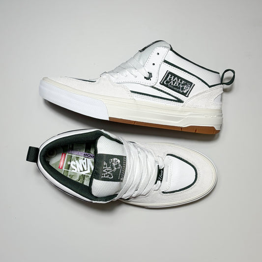 A pair of white Vans Skate Half Cab Wafflecup Una Farrar sneakers shown from different angles on a light gray background. One shoe is positioned upright, showing the side profile with its signature black stripe and Cactus patch, while the other is laid flat, showing the top view with white laces and a black tongue label.