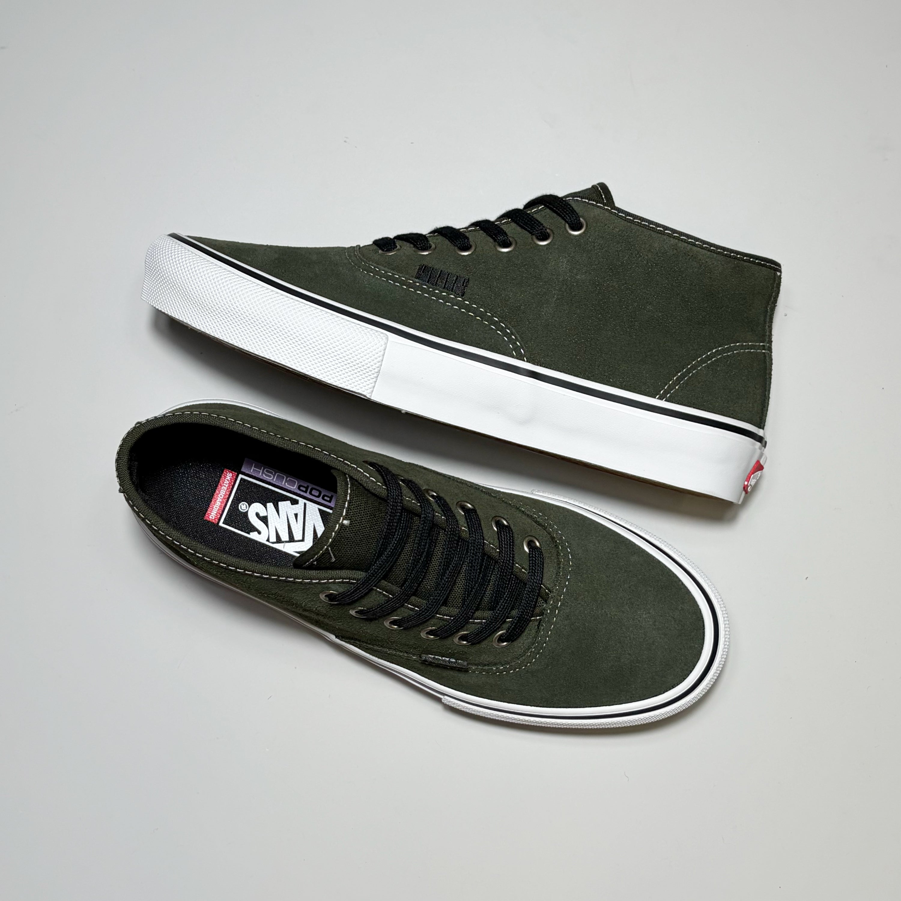 A pair of Vans Skate Authentic Mid sneakers in dark olive green suede with black laces and white rubber soles, displayed on a light gray background.
