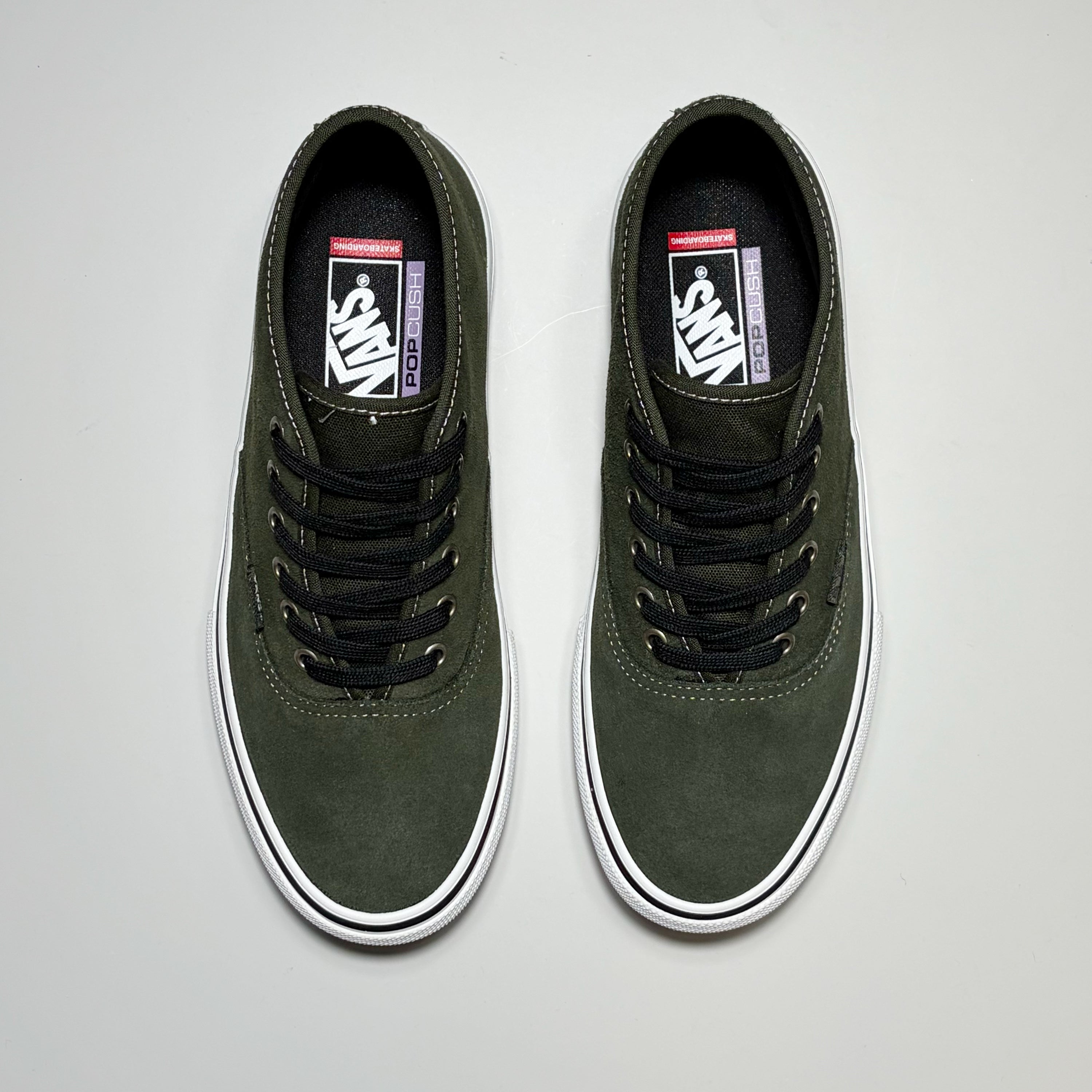 A pair of Vans Skate Authentic Mid shoes in dark olive green suede, featuring black laces and white rubber soles, photographed from a top-down perspective on a light gray background.