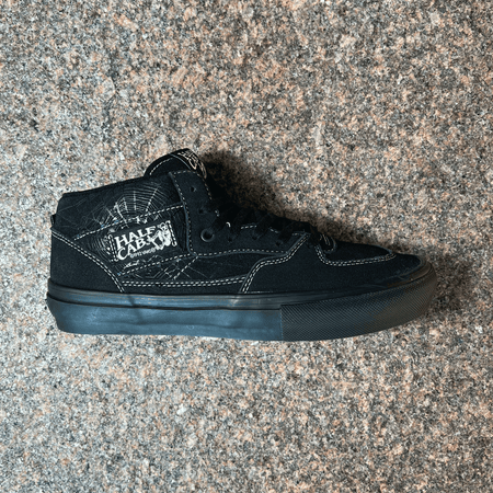 SIDE VIEW OF THE VANS HALF CAB SHOE IN BLACK SUEDE AND WHITE STITCHING WITH BLACK SOLE. WEB PRINTED GRAPHIC ON THE BACK PANEL DISPLAYED ON GRANITE