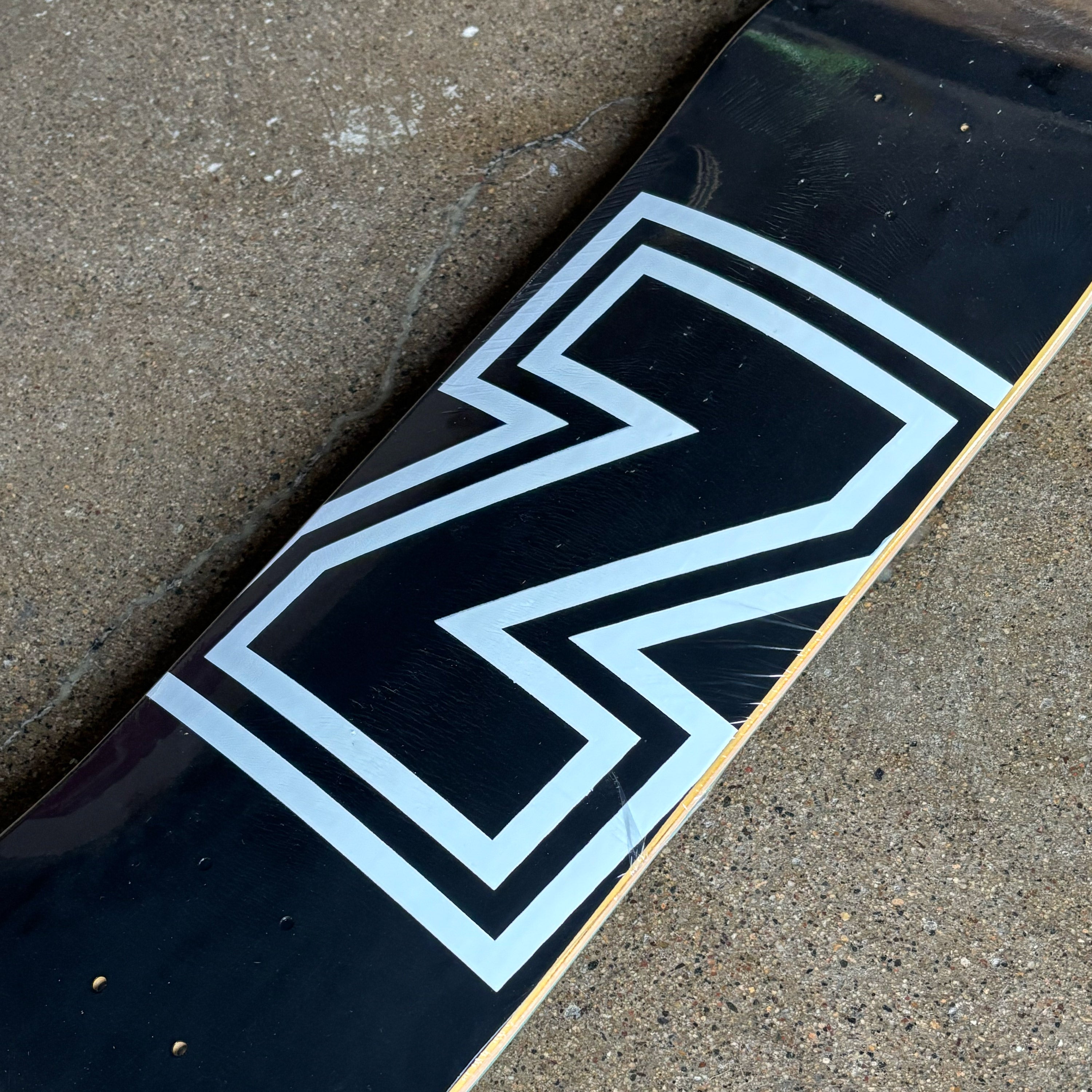 Close-up of a skateboard deck with a logo on a concrete surface