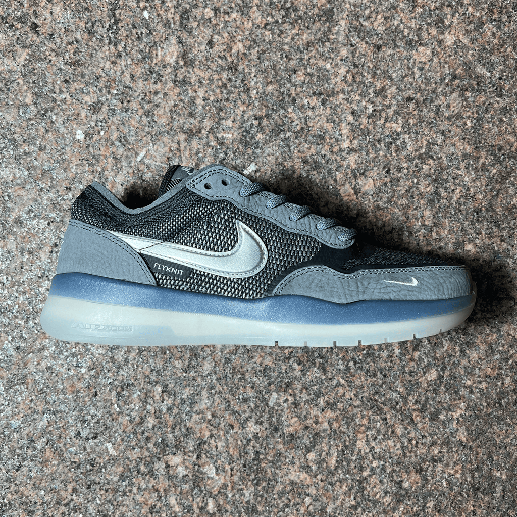 SINGLE NIKE SB PS8 FLYKNIT SHOE IN COOL GREY WITH SUEDE PANELING, CLEAR SOLE AND METALLIC SWOOSH DISPLAYED ON GRANITE