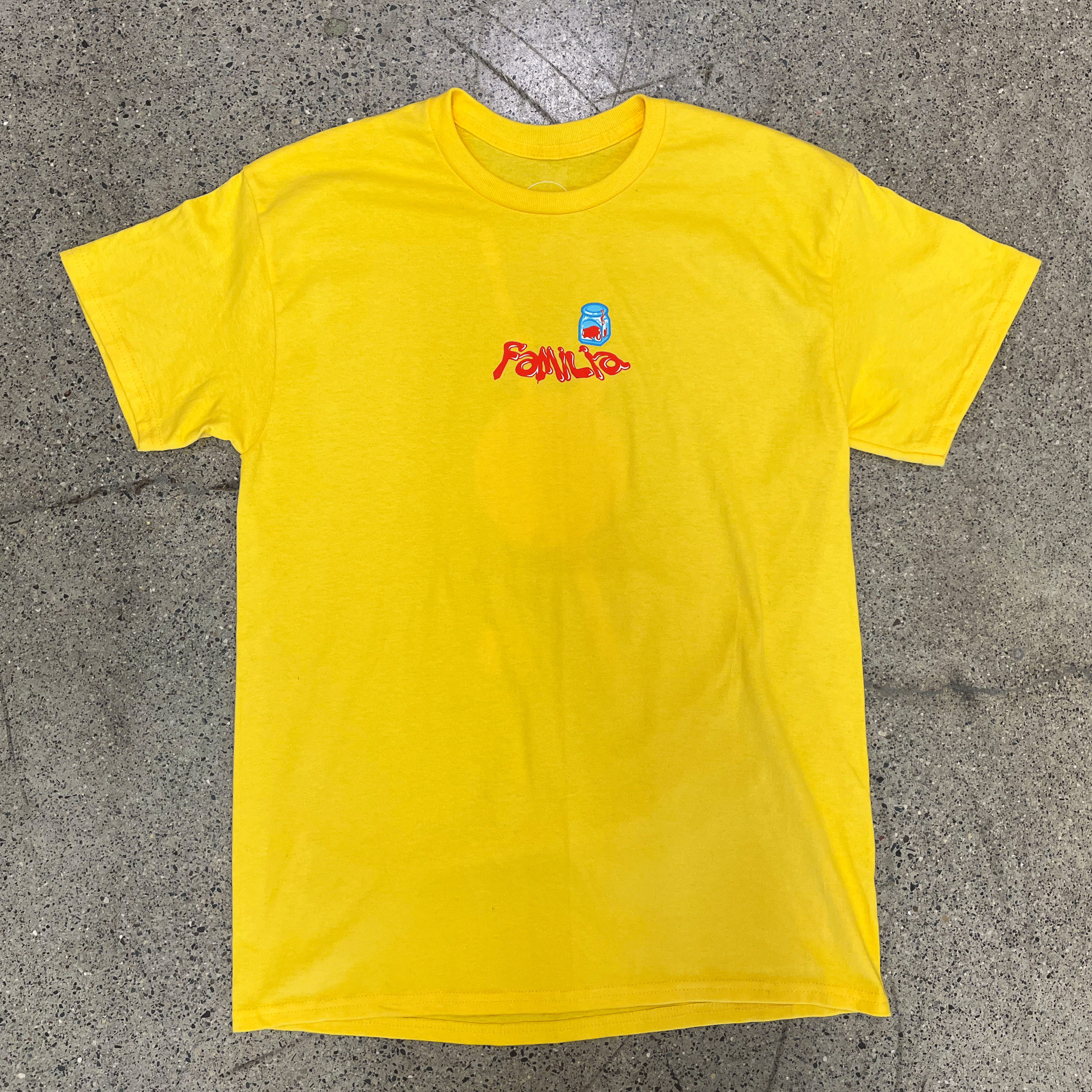 FRONT SIDE OF YELLOW T-SHIRT WITH GRAPHIC OF A PEN FOUNTAIN AND FAMILIA IN LIQUID FONT ON THE CHEST