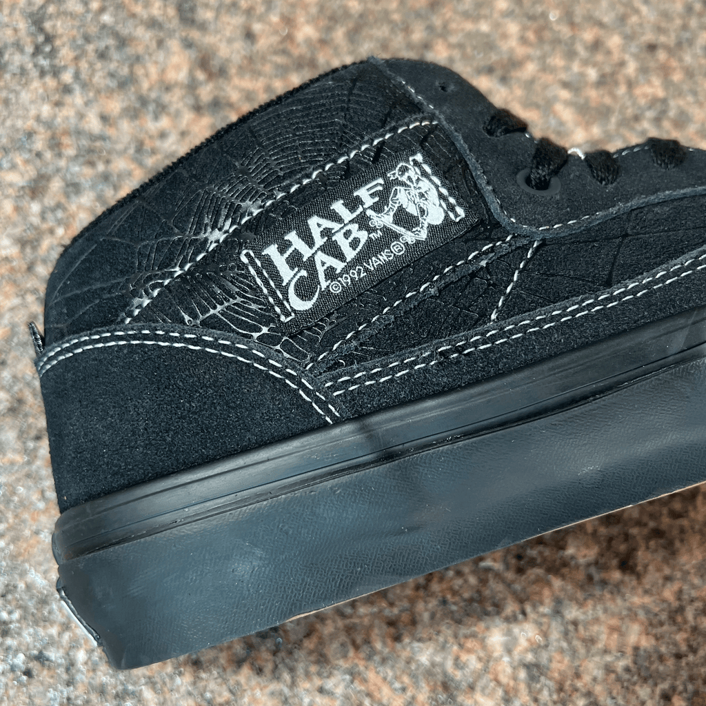 SIDE VIEW OF THE VANS HALF CAB SHOE IN BLACK SUEDE AND WHITE STITCHING WITH BLACK SOLE. WEB PRINTED GRAPHIC ON THE BACK PANEL DISPLAYED ON GRANITE